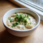 A white bowl filled with creamy keto white chicken chili, topped with shredded cheese, sour cream, and fresh cilantro.