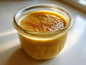 Close-up of thick, creamy maple mustard salad dressing in a glass jar, lightly dusted with spice.