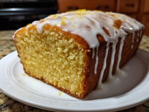 A moist lemon loaf, cut to show the crumb, topped with thick white glaze and lemon zest.