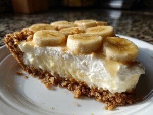 A close-up of a thick slice of no-bake banana cream pie showing the graham cracker crust, creamy filling, and sliced bananas on top.