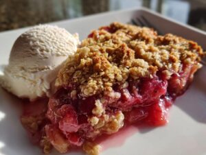 A warm slice of rhubarb crisp topped with a scoop of vanilla ice cream, showing gooey filling.