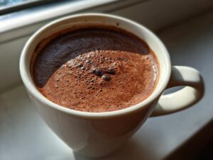 Close-up of a creamy, dark brown french hot chocolate with small bubbles on the surface in a white mug.