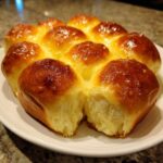 A cluster of golden brown, soft sourdough discard rolls pulled apart on a white plate.