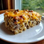 A hearty slice of sour cream beef noodle casserole topped with melted cheddar cheese, served on a white plate.