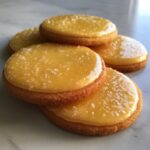 Close-up of round sugar cookies topped with glossy, yellow sugar cookie icing that hardens, sprinkled with coarse salt.