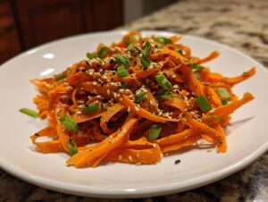 Close-up of a vibrant raw carrot salad made with shaved carrots, topped with sesame seeds and green onions.