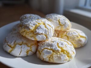 A stack of bright yellow lemon crinkle cookies heavily dusted with white powdered sugar on a white plate.