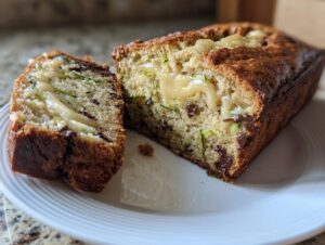 A loaf of zucchini banana bread sliced open, revealing shredded zucchini, chocolate chips, and a gooey cream cheese swirl.