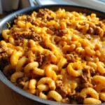 Close-up shot of creamy elbow macaroni mixed with seasoned ground beef and melted cheddar cheese in a skillet, showing the finished taco pasta.