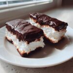 Two rectangular bars of homemade cool whip candy, featuring a dark chocolate coating over fluffy white filling and a bottom crust.