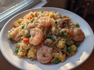 A close-up of delicious shrimp fried rice featuring plump shrimp, scrambled egg, peas, and carrots on a white plate.