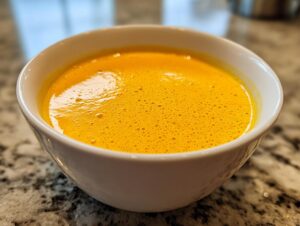 Close-up of bright orange, slightly foamy cottage cheese queso served in a small white bowl on a granite countertop.