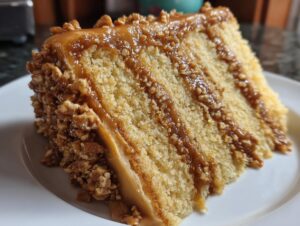A close-up of a tall slice of caramel crunch cake showing multiple layers and crunchy nut coating.