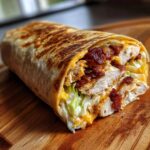 A cross-section view of a perfectly grilled chicken bacon ranch wrap showing sliced chicken, crispy bacon, lettuce, and ranch dressing.