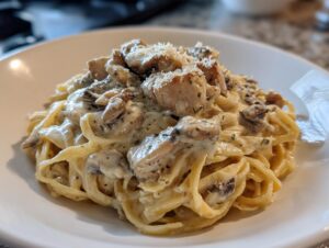 A close-up of creamy chicken fettuccine alfredo pasta topped with mushrooms and grated Parmesan cheese.