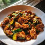 A close-up of glistening chicken zucchini stir fry coated in a savory brown sauce, served in a white bowl.