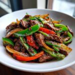 Close-up of vibrant Chinese pepper steak with beef, green peppers, red peppers, and onions coated in dark sauce.