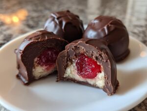 Close-up of homemade chocolate covered cherries, one cut in half showing the cherry center and white filling.