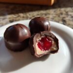 Three homemade chocolate covered cherries, one cut open to show the creamy filling and bright red cherry center.