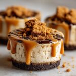 Close-up of a single cookie butter cheesecake cup drizzled with caramel and chocolate, topped with cookie crumbs.