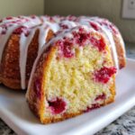 Close-up of a slice of moist cranberry orange cake showing bright red cranberries baked inside, topped with a white citrus glaze.