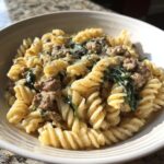Close-up of a bowl of creamy beef pasta made with fusilli, ground beef, and wilted spinach.