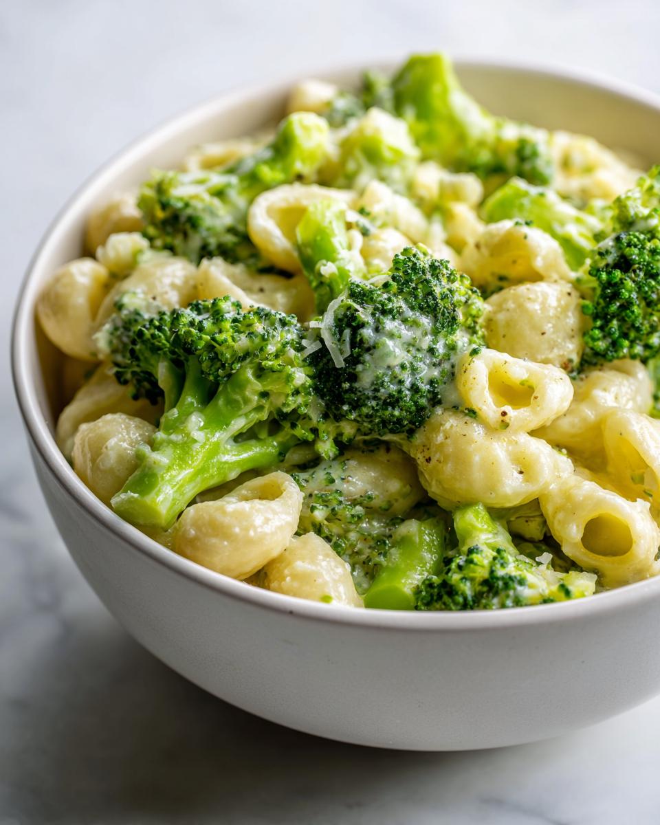 Close-up of creamy broccoli pasta featuring bright green florets and shell pasta coated in a rich sauce, served in a white bowl.