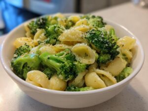Close-up of a white bowl filled with creamy broccoli pasta, featuring shell pasta and bright green florets topped with Parmesan.