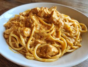 Close-up of a serving of creamy cajun chicken pasta coated in a rich, orange sauce, featuring chunks of chicken and spaghetti noodles.