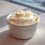 A small white ramekin filled with thick, fluffy creamy horseradish sauce, sitting on a light wooden surface.
