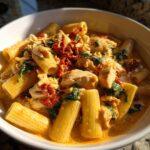 Close-up of creamy marry me chicken pasta with rigatoni, chicken chunks, sun-dried tomatoes, and spinach.