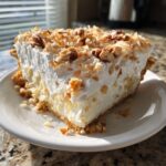 A thick slice of creamy Million Dollar Pie topped with toasted coconut and pecans on a white plate.