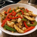 Close-up of seasoned chicken strips mixed with sautéed red and green bell peppers and onions for crockpot chicken fajitas.