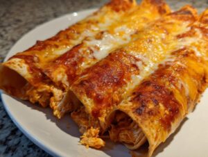Three baked easy chicken enchiladas covered in red sauce and melted golden cheese on a white plate.