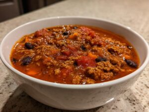 A close-up of a white bowl filled with rich, thick pumpkin chili featuring ground meat, black beans, and diced tomatoes.