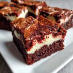 A close-up of a fudgy red velvet cheesecake brownies square showing the distinct red layer and creamy white cheesecake swirl.