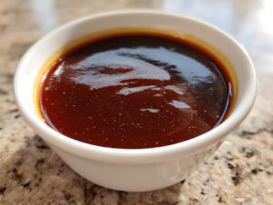 Close-up of rich, dark homemade brown gravy served in a small white ramekin on a granite countertop.