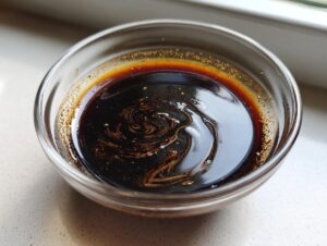 Close-up of thick, dark homemade teriyaki sauce swirling in a small clear glass bowl.