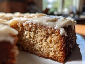 A close-up, macro shot showing the moist, textured crumb of a slice of applesauce cake topped with creamy frosting.