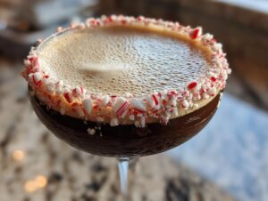 Close-up of a rich, dark peppermint espresso martini topped with foam and a crushed candy cane rim.