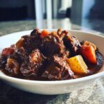 Close-up of tender chunks of meat and vegetables in a rich gravy, classic crockpot beef stew served in a white bowl.