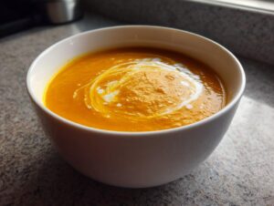 A close-up of vibrant orange roasted butternut squash soup, swirled with cream, served in a white bowl.