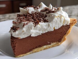 A close-up of a perfect slice of french silk pie featuring a thick chocolate filling, topped with whipped cream and chocolate shavings.