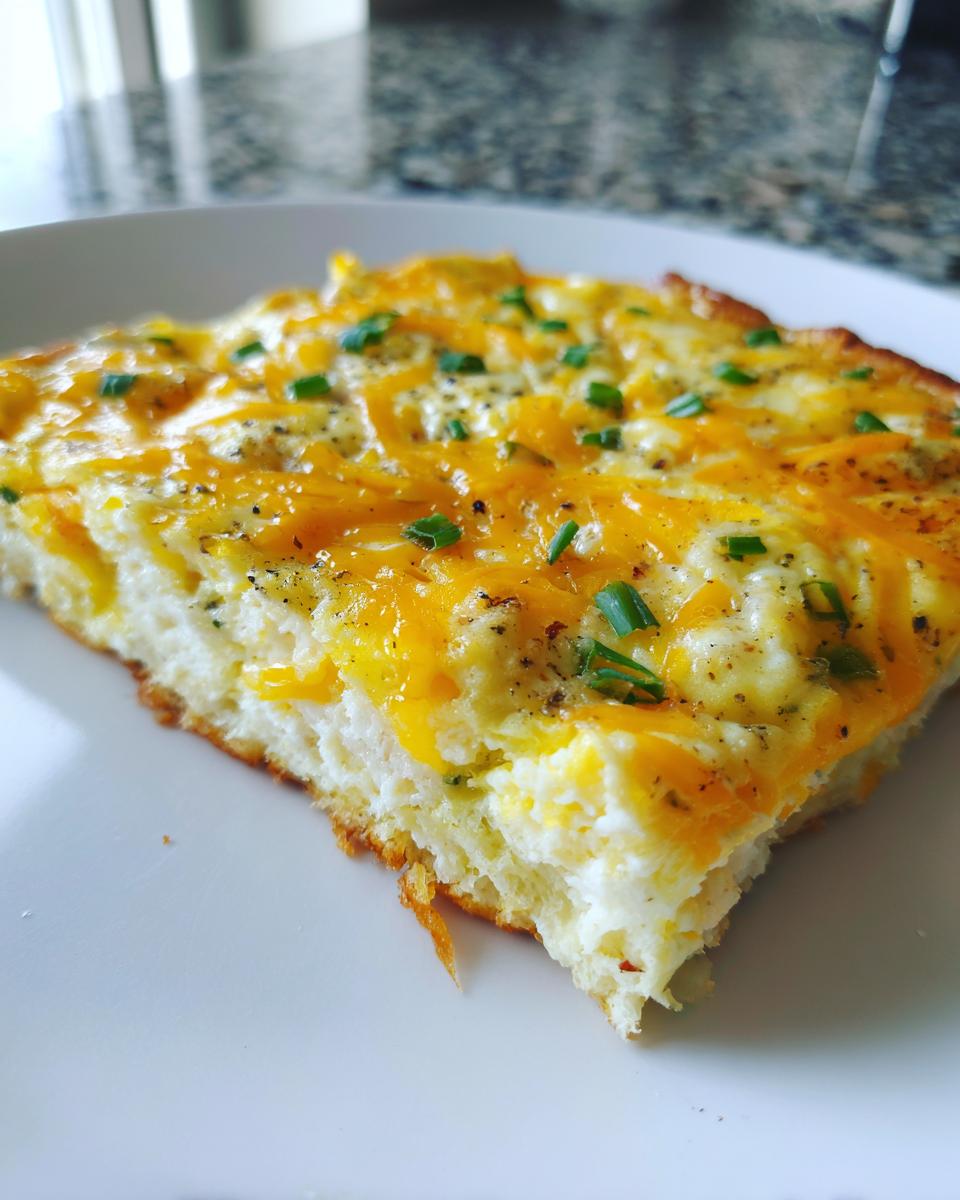 Close-up of a square slice of fluffy sheet pan eggs topped with melted cheddar cheese and fresh chives.