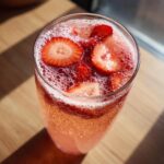 Close-up overhead view of a glass filled with fizzy strawberry champagne punch garnished with fresh strawberry slices.