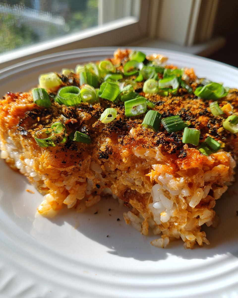 A close-up serving of baked sushi bake, showing the creamy rice base and savory topping garnished with fresh chopped green onions.