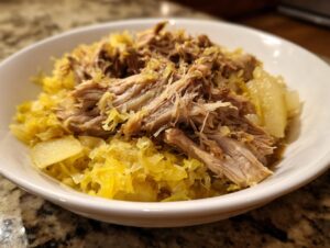 Close-up of tender, shredded pork served over bright yellow pork and sauerkraut in a white bowl.