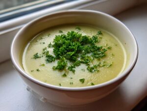 A close-up of a bowl of smooth, velvety celery soup topped with bright green chopped parsley.