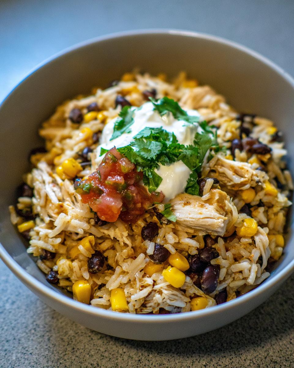 Close-up of a hearty chicken burrito bowl with seasoned rice, black beans, corn, topped with sour cream, salsa, and cilantro.