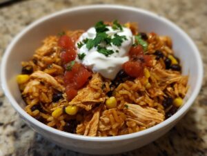 Close-up of an amazing chicken burrito bowl with seasoned rice, shredded chicken, black beans, corn, salsa, and sour cream.